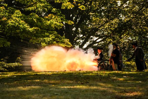 A cannon firing with a massive flame shooting out the muzzle of the gun.