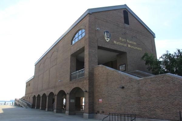 A three-story brick structure with a staircase in front and water in the background