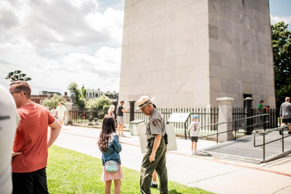 A young kid listening to a Ranger speak in front of a granite monument.
