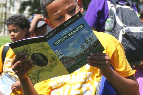 An African American child holding up the "Liberty Junior Ranger Activity Book."