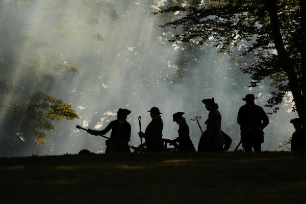A group of people dressed as Revolutionary War artillery soldiers are working on a cannon