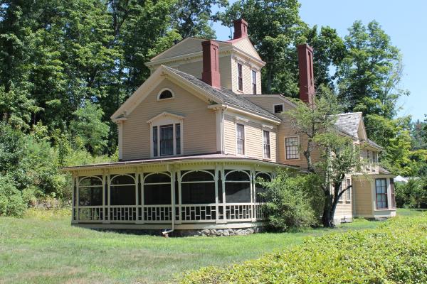 A yellow wooden house with wrap around porch and 3 story central tower