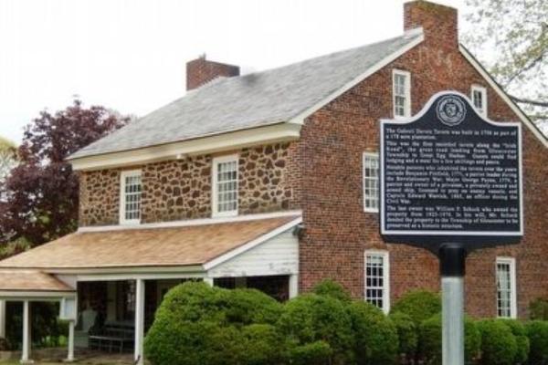 A historic stone-and-brick tavern with white trim stands behind a black marker describing its 1756 origins.
