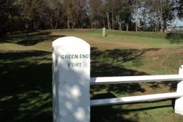 A white stone marker labeled “Green End Fort” stands in a grassy landscape with bare trees and a bright blue sky.
