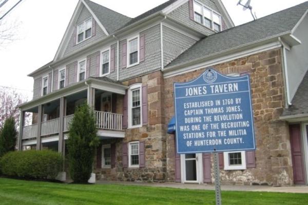 A stone‑and‑shingle historic building with a columned porch stands behind a blue marker identifying it as Jones Tavern, established in 1760.