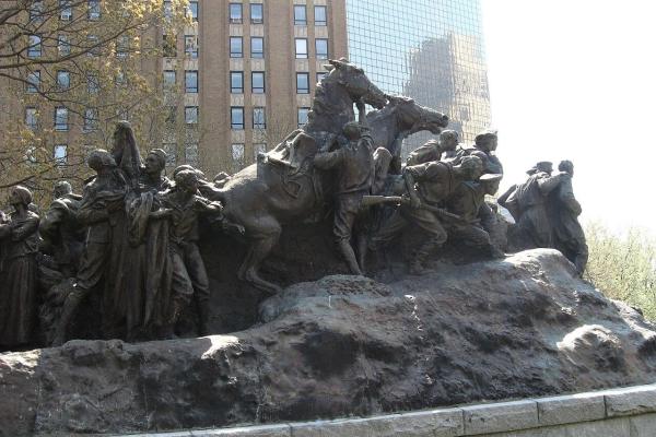 A large bronze monument shows soldiers and civilians in dramatic motion, with horses and figures emerging from a rugged base in an outdoor urban park.