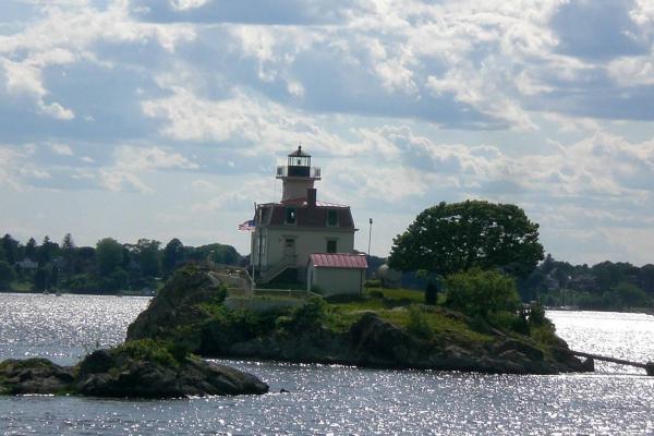 A small rocky island with a cream-colored lighthouse and red roof surrounded by water.