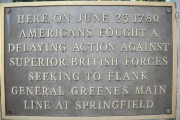 A bronze plaque mounted on a stone surface commemorates a June 23, 1780 battle where Americans delayed advancing British forces near Springfield.