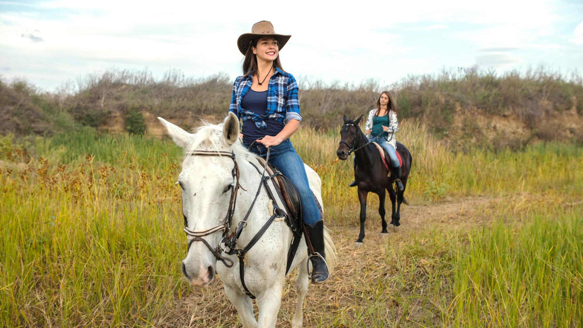 two women riding horseback in a field