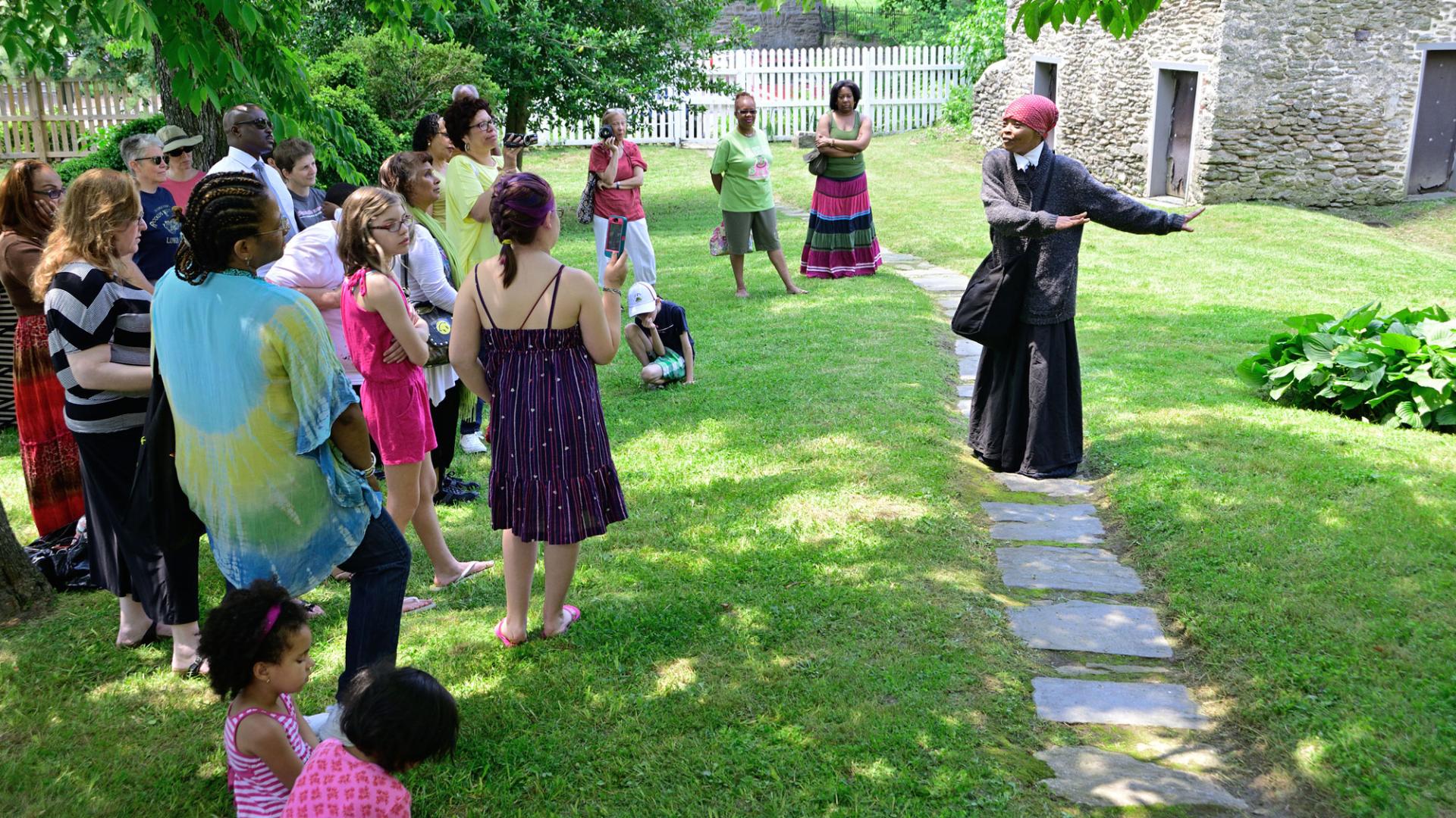 A costumed woman speaks in front of a group of tourists outside