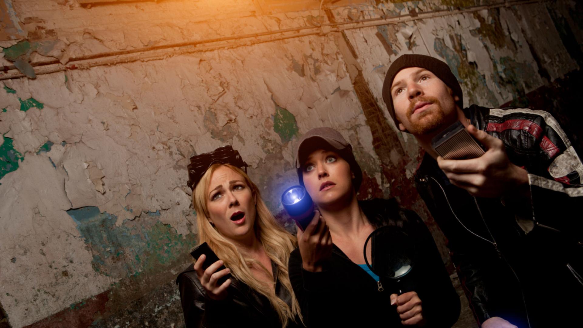 Image of 2 women and 1 man in a dark interior with flashlights