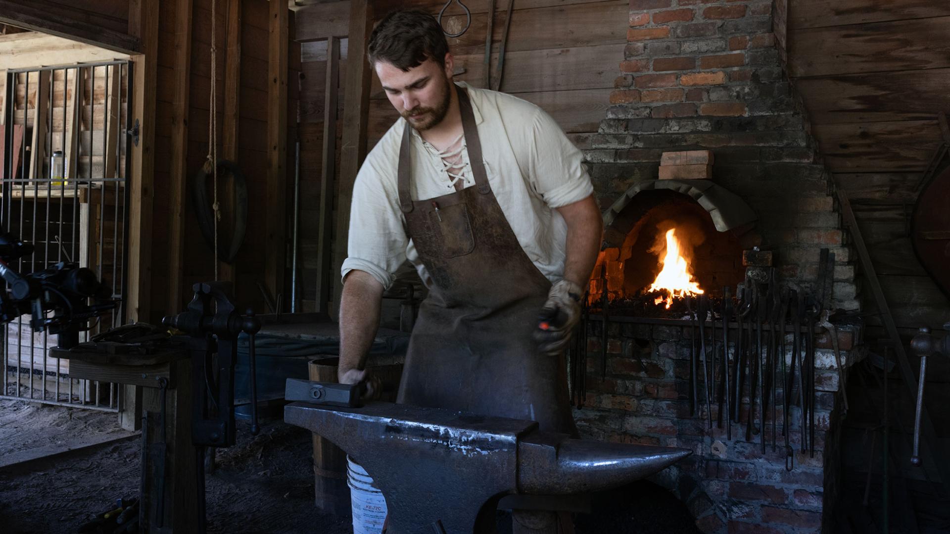a man forges iron objects in front of an open fire