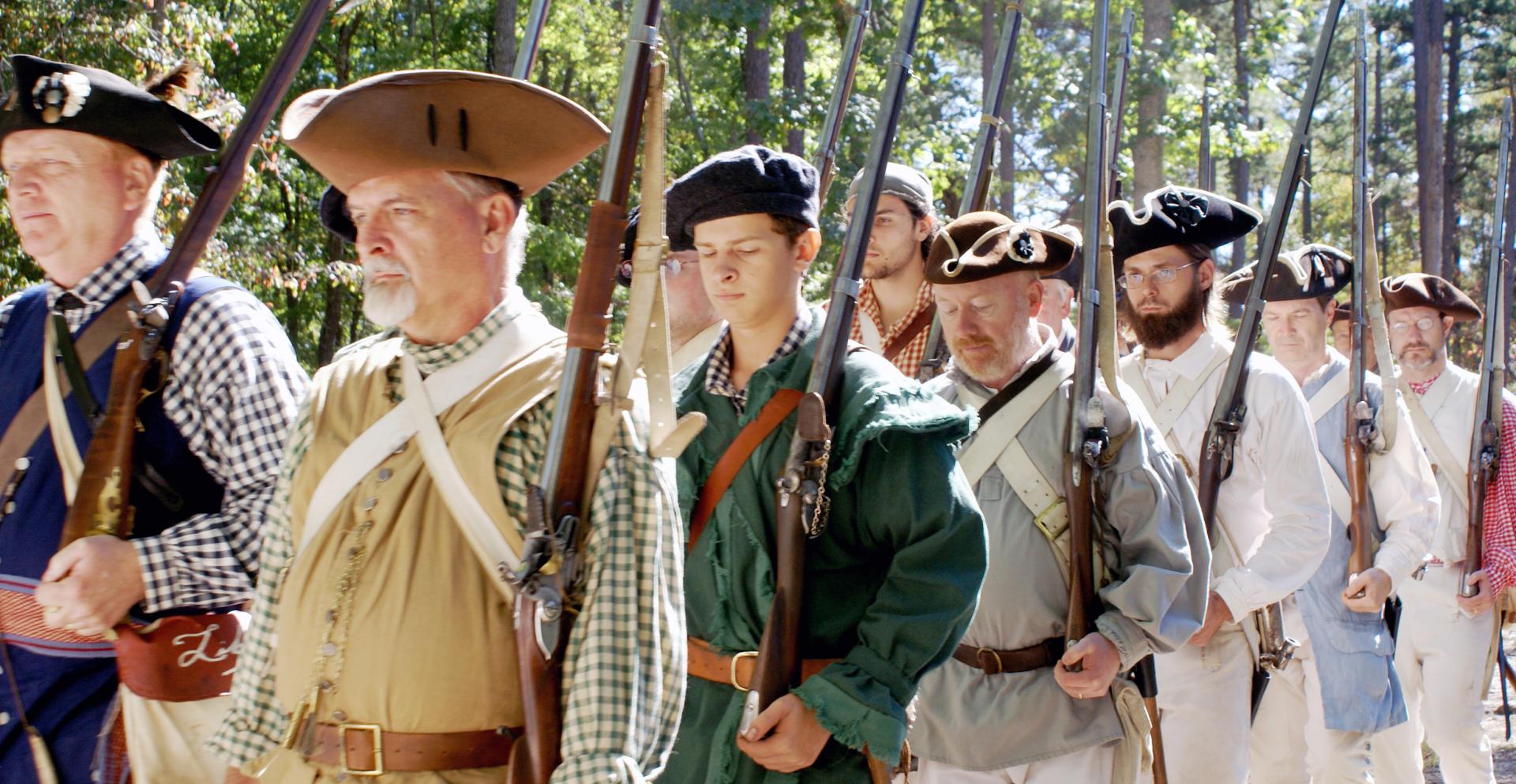 Militia reenactors march with weapons on their shoulders as they prepare to demonstrate them.