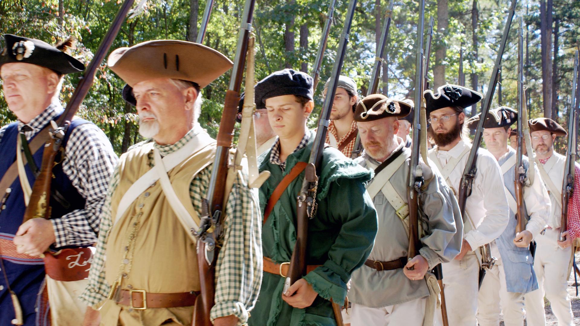 Militia reenactors march with weapons on their shoulders as they prepare to demonstrate them.