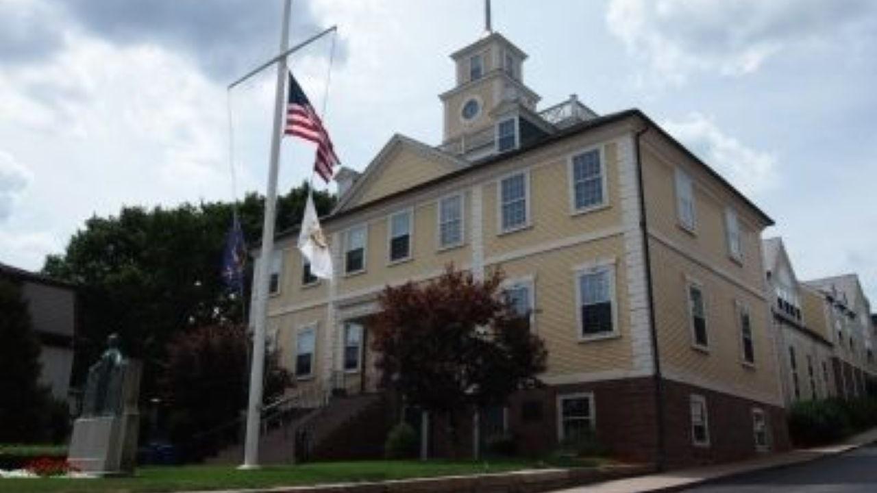 A historic yellow civic building stands behind a flagpole flying the American flag.