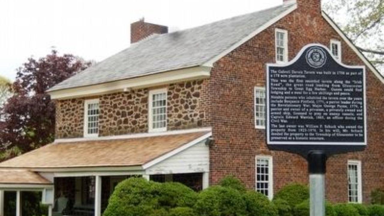 A historic stone-and-brick tavern with white trim stands behind a black marker describing its 1756 origins.