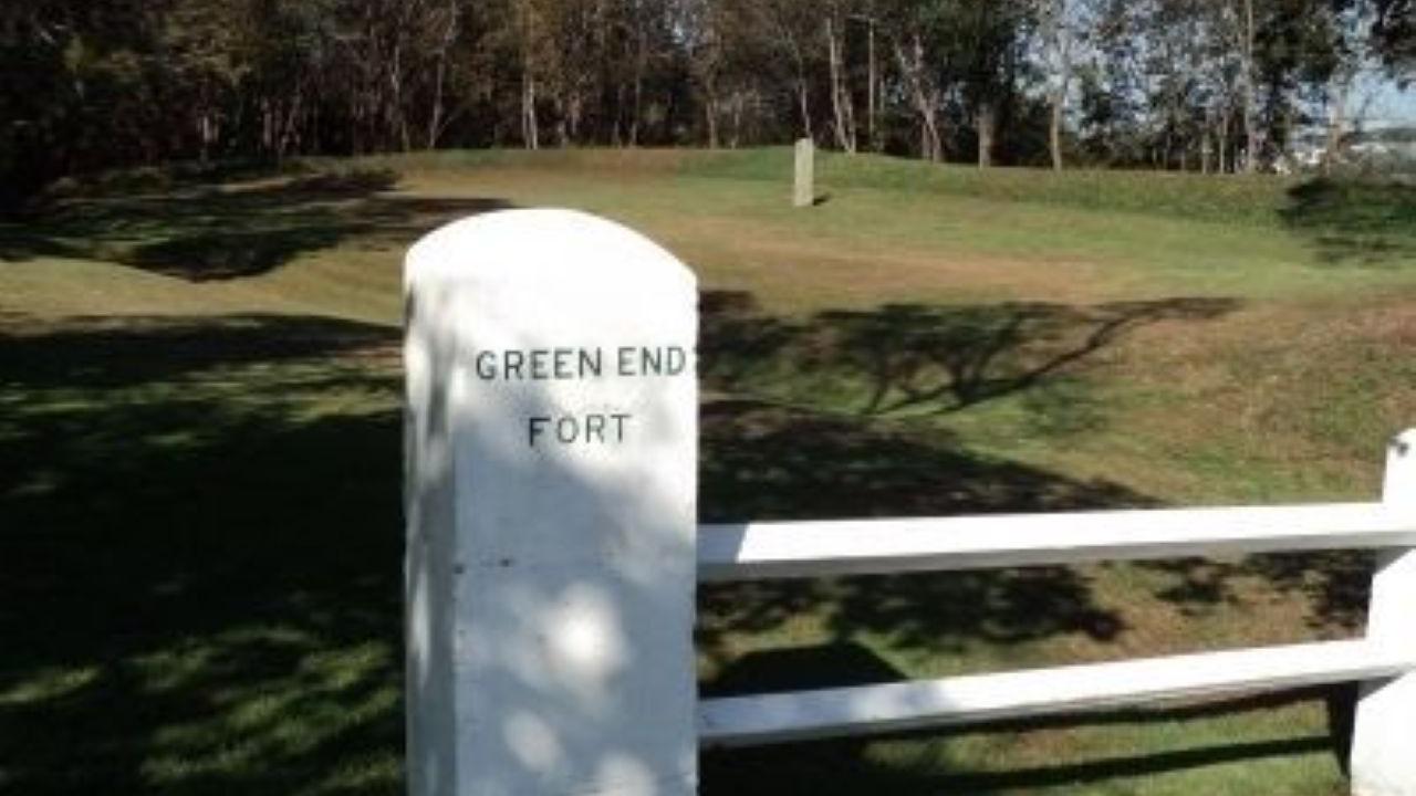 A white stone marker labeled “Green End Fort” stands in a grassy landscape with bare trees and a bright blue sky.