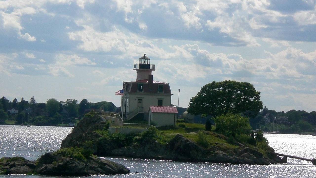 A small rocky island with a cream-colored lighthouse and red roof surrounded by water.