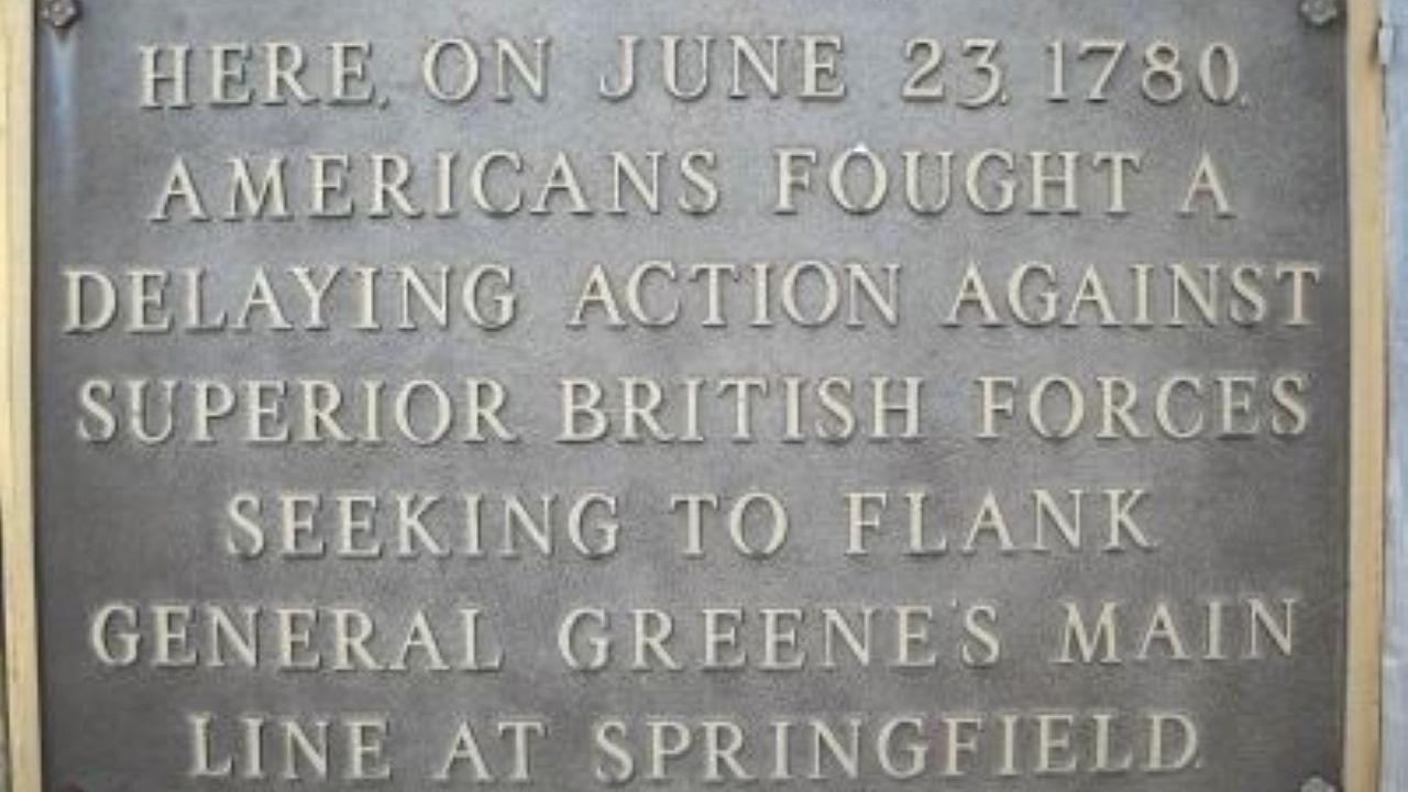 A bronze plaque mounted on a stone surface commemorates a June 23, 1780 battle where Americans delayed advancing British forces near Springfield.