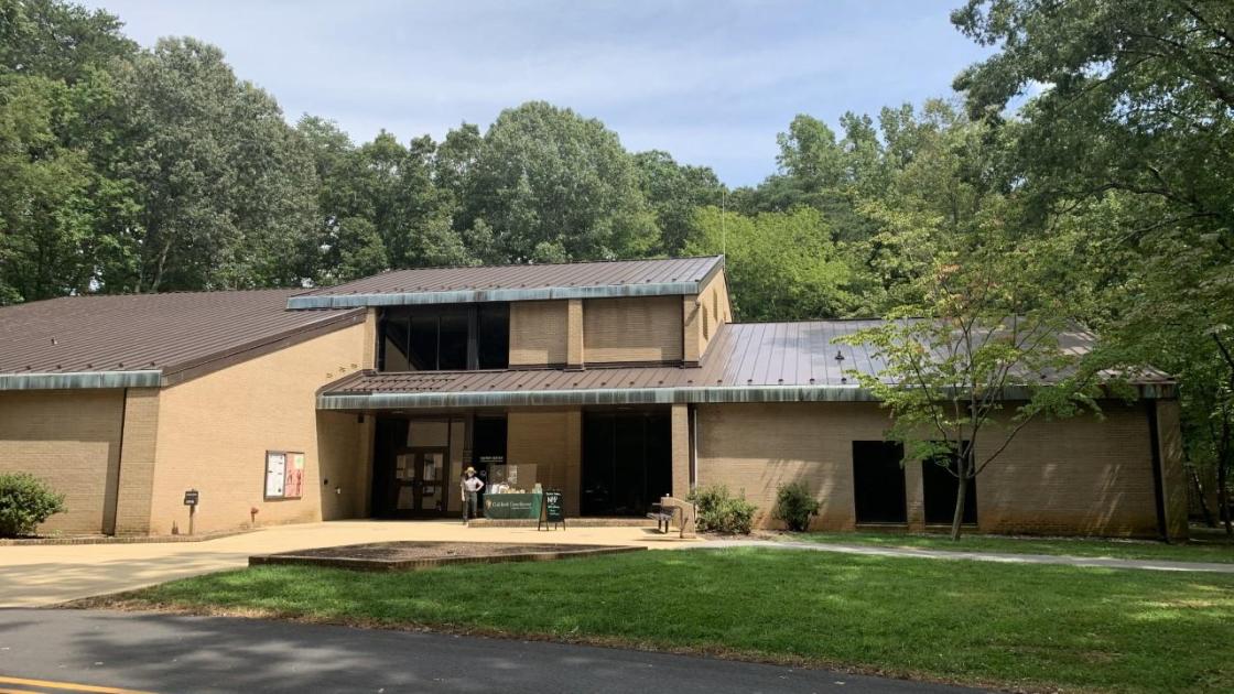 Modern brown building surrounded by trees, park ranger standing in front