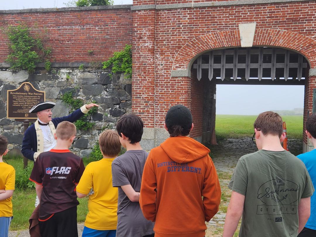 A man dressed as a Patriot reenactor gives a tour of a fort to a group of Boy Scouts.